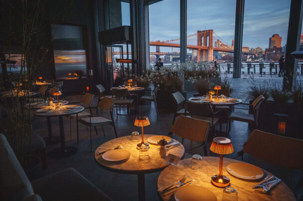 A nighttime view from the restaurant showcasing tables and chairs illuminated by soft lighting. - Hausion