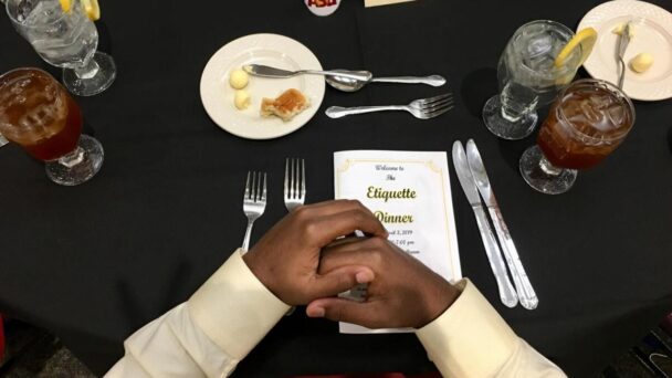 A man extends his hand over a table, showcasing a plate of food in front of him. - Hausion