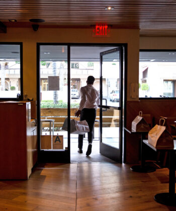 A person walking through a restaurant, navigating between tables and patrons in a lively dining atmosphere. - Hausion