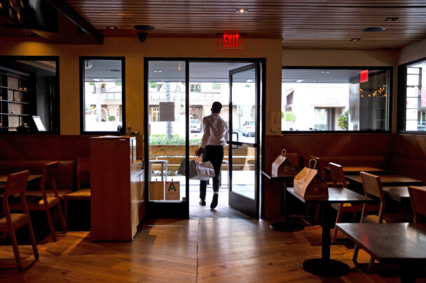 A person walking through a restaurant, navigating between tables and patrons in a lively dining atmosphere. - Hausion