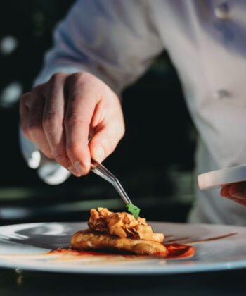 A chef skillfully arranges food on a plate in a restaurant kitchen, showcasing culinary artistry and attention to detail. - Hausion