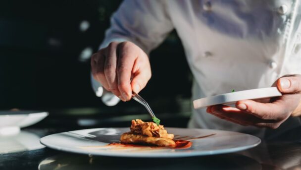 A chef skillfully arranges food on a plate in a restaurant kitchen, showcasing culinary artistry and attention to detail. - Hausion