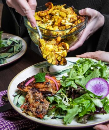 A person serves food onto two plates, showcasing a meal being prepared for sharing. - Hausion