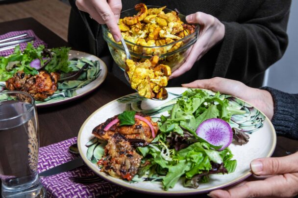 A person serves food onto two plates, showcasing a meal being prepared for sharing. - Hausion