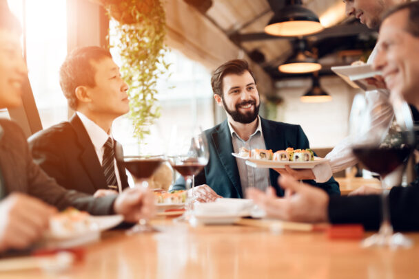 Businessmen engaged in conversation while dining together at a restaurant, showcasing a professional networking atmosphere. - Hausion