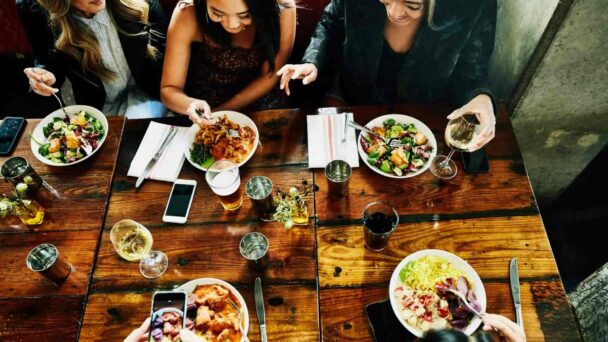 A diverse group of individuals enjoying a meal together at a table filled with various dishes. - Hausion