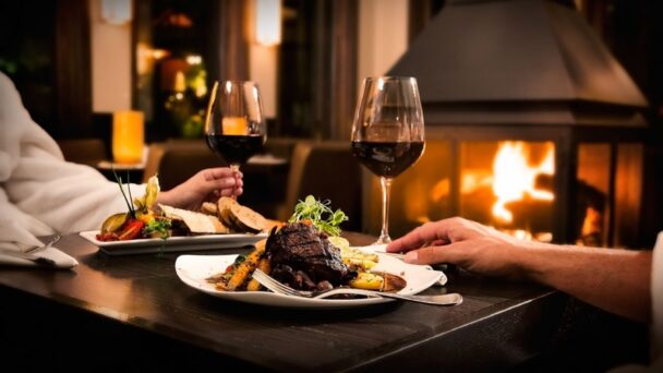 Two individuals in bathrobes share a joyful moment, raising wine glasses and indulging in tasty dishes. - Hausion