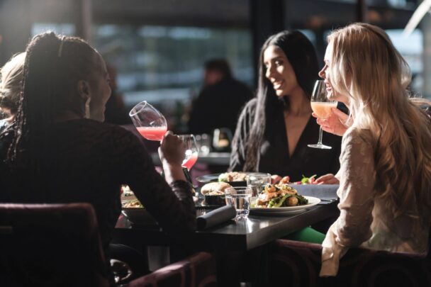 Three women share laughter and delicious food together at a cozy restaurant table, enjoying their meal and each other's company. - Hausion