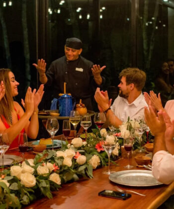 A lively group of friends at a table, hands raised in excitement, sharing joyful moments together. - Hausion