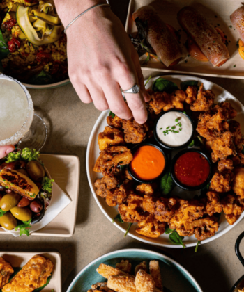 A lively table filled with delicious food as friends enjoy their meal and drinks together, creating joyful moments. - Hausion