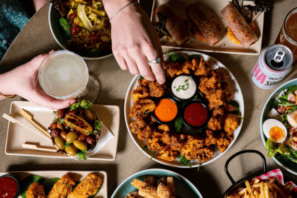 A lively table filled with delicious food as friends enjoy their meal and drinks together, creating joyful moments. - Hausion