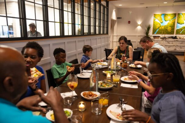 A lively group of friends enjoying a meal together at a cozy restaurant, sharing laughter and delicious food. - Hausion