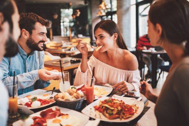 A cheerful group of friends enjoying a delicious breakfast together at a cozy restaurant, sharing laughter and good food. - Hausion