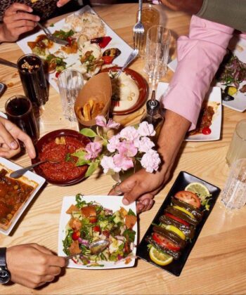 A lively group of friends gathered around a table, enjoying a delicious spread of food and sharing joyful moments together. - Hausion