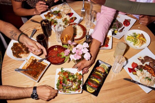 A lively group of friends gathered around a table, enjoying a delicious spread of food and sharing joyful moments together. - Hausion